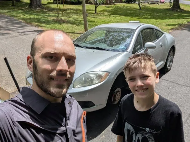 Ed and Zack smiling next to a car with a front wheel off