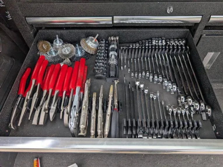 An organized drawer of pliers, wrenches and wire brushes